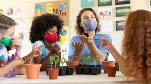 Female teacher wearing face mask showing plant pots to students in class