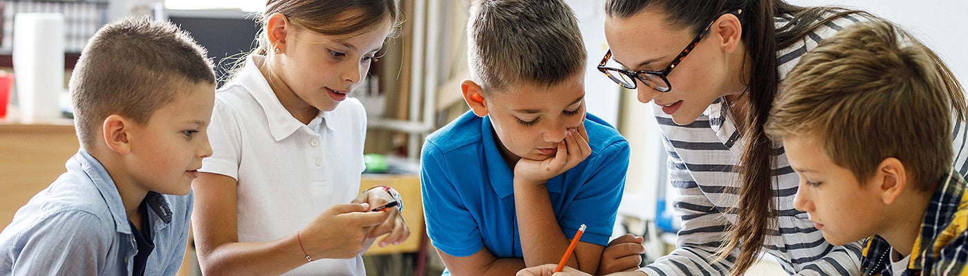 Teacher giving instruction to grade school children at a desk