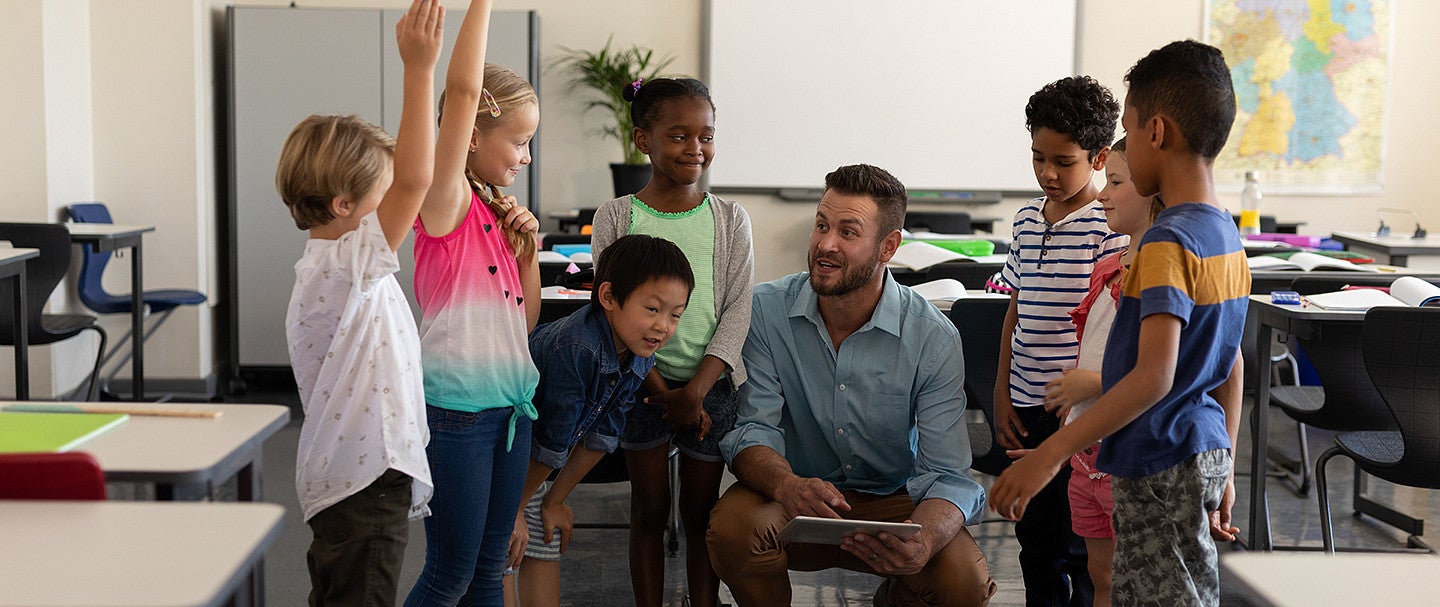 Classroom with teacher speaking to a groups of smiling children gathered around him