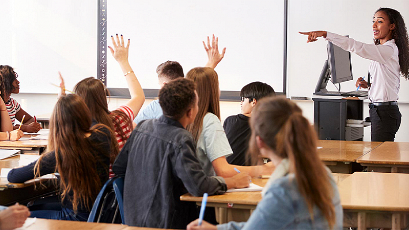 High school students raising their hands as a teacher calls on them  