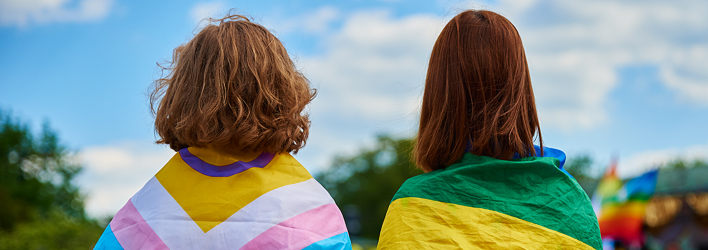 Two students with their backs turned, drapped in rainbow flags