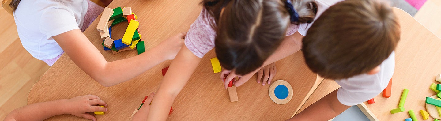 Preschool teacher with children playing with colorful wooden didactic toys at kindergarten